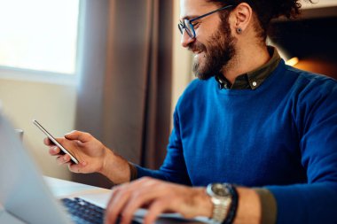 Çekici beyaz sakallı girişimci ofisinde oturuyor, akıllı telefon kullanıyor ve işe ara veriyor..