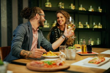 Genç, beyaz tenli bir çift restoranda oturup beyaz şarapla tost yapıyorlar..