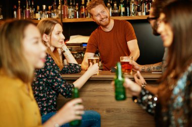 Genç yakışıklı barmen müşterilerle konuşuyor. Bar içi..