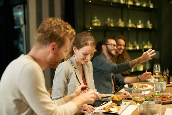Молодая пара делится едой в ресторане, пока другая пара делает селфи
.
