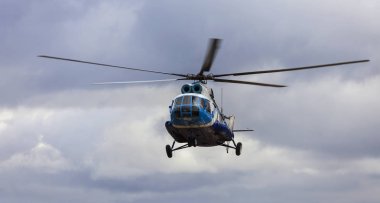 Bulutlu bir gökyüzüne karşı mavi ve beyaz renklerde helikopter.