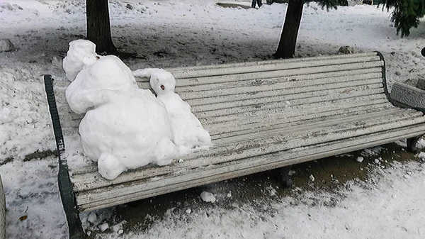 Two melted snowmen on a bench in the park.