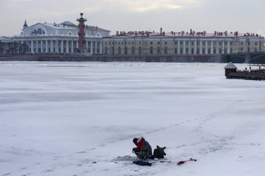 St. Petersburg 'un merkezindeki Neva nehri buzunda buz balıkçılığı. Bir balıkçı, Rusya 'nın kuzey başkentinin tarihi merkezinde Vasilievsky adası ve Rostral sütunlarının arka planında balık yakalar.