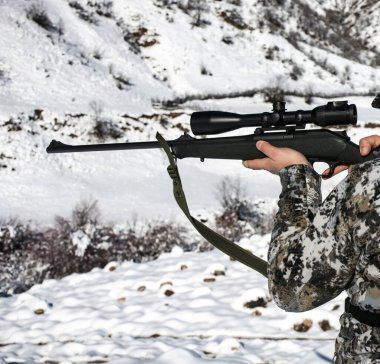Kış kamuflajlı bir avcı optiğe nişan alır. Kış kamuflajlı bir adam dağlarda av tüfeği ateşlemeden önce teleskopik bir görüntüye bakar.. 