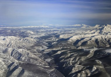 İlkbaharda uçaktan Kamçatka Yarımadası 'nın dağlarının manzarası. Uçak penceresinden Kamçatka dağları ve Klyuchevskaya Sopka volkanı patlaması. 
