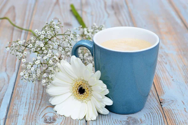Cup of coffee in a blue mug on a old used grey wooden background with a white Gerber daisy decoration — Stock Photo, Image
