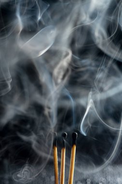 Siyah arka planda yanan üç kibrit çöpü ve duman.