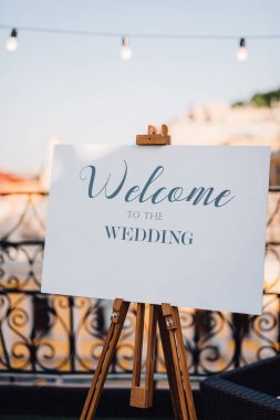 Easel with white board with lettering 'Welcome to the wedding' stands on the balcony clipart