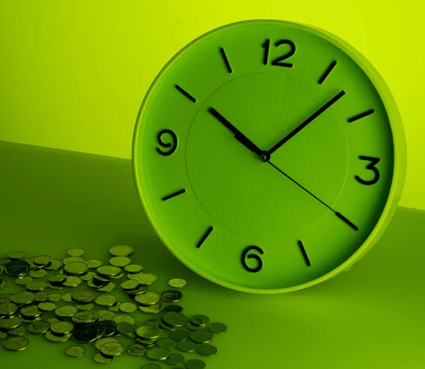 White clock and silver coins on green background