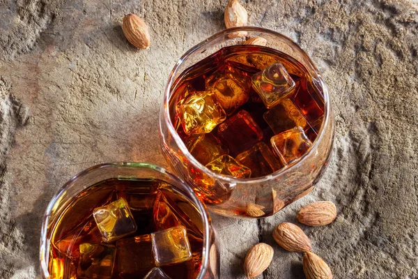 Two glasses whiskey bourbon with ices and almonds on old wooden table — Stock Photo, Image