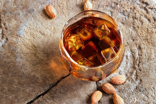 Whiskey bourbon with ices in glass and almonds on old wooden — Stock Photo, Image
