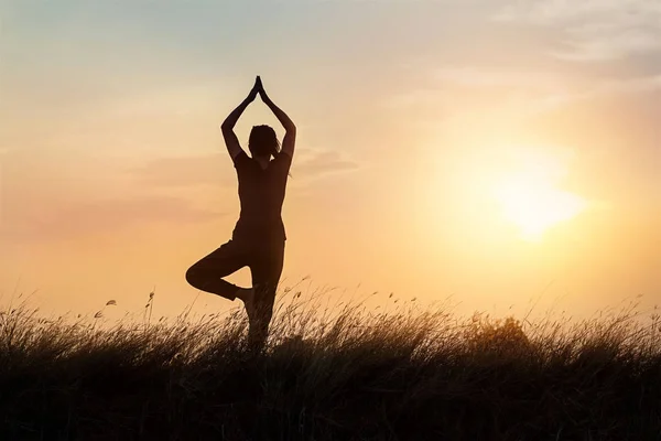 Silueta de mujer practicando yoga sobre la naturaleza en el fondo del atardecer —  Fotos de Stock