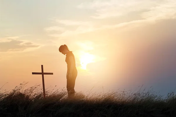 Donna rispettando alla croce sul campo di sfondo tramonto — Foto Stock