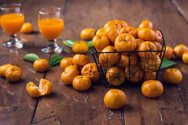 Orangen Früchte im Korb und ein Glas Orangensaft auf Holz — Stockfoto