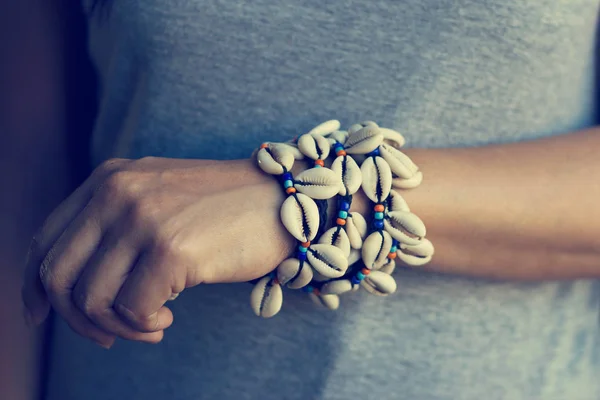 Cowrie shell bracelets on the wrist of woman, vintage color tone — Stock Photo, Image