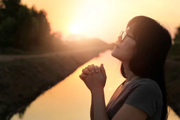Mujer rezando con las manos juntas sobre el fondo de la puesta del sol naturaleza —  Fotos de Stock
