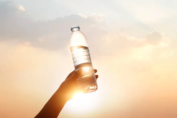 Ręka trzyma wody pitnej na tle zachodu słońca — Zdjęcie stockowe