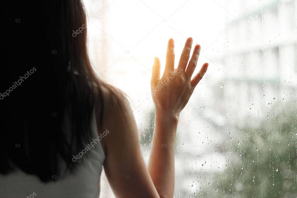 Sad woman looking through the glass window with rain drops 