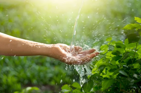 Wasser ergießt sich in Frauenhand auf Naturhintergrund, Umweltthema — Stockfoto