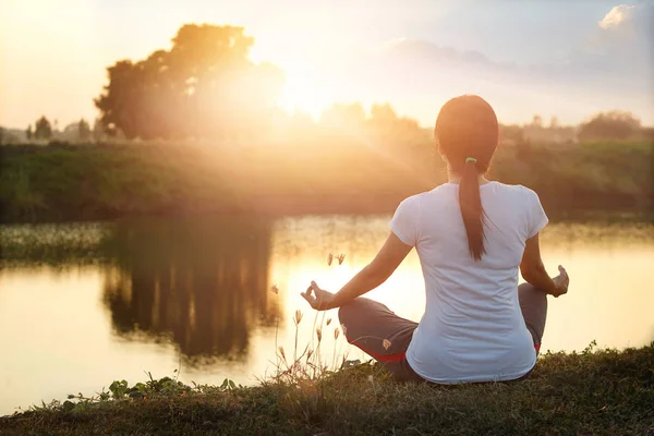 Mujer joven practicando yoga y meditando junto al lago en verano —  Fotos de Stock