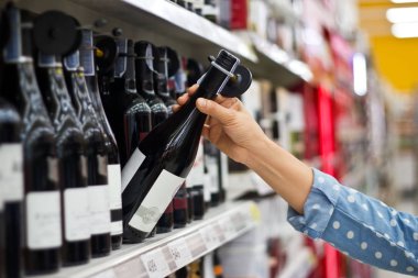 Kadın bir şişe şarap süpermarket arka planda satın alıyor