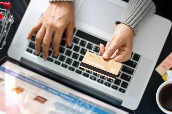 Conceito de compras online. Mãos de mulher segurando cartão de crédito ouro para compras on-line usando laptop em casa. Vista superior — Fotografia de Stock