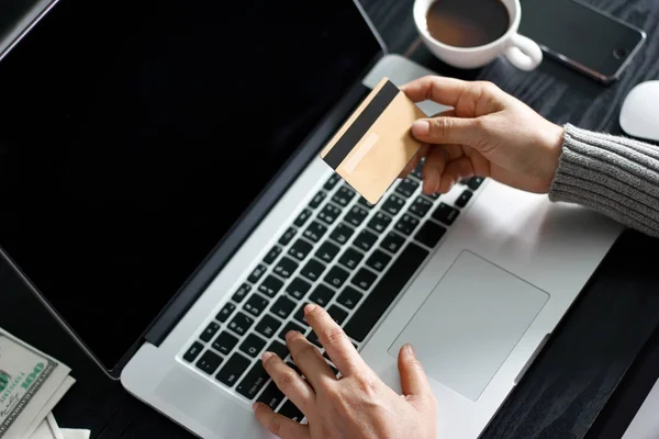 Conceito de compras online. Mãos de mulher segurando cartão de crédito ouro na mão para compras on-line usando laptop em casa . — Fotografia de Stock