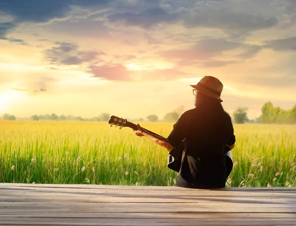 Woman playing acoustic guitar on the field rural sunset background — Stock Photo, Image
