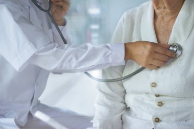 Steteskop analizi yapan kardiyolog doktor ve hastane geçmişinde kalp atışlarını kontrol eden yaşlı kadın.