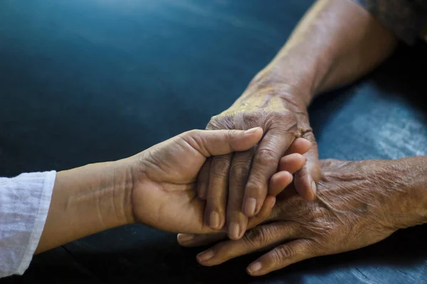 Dotter håller hand mor äldre som är alzheimer och parkinson patient på mörk bakgrund. — Stockfoto