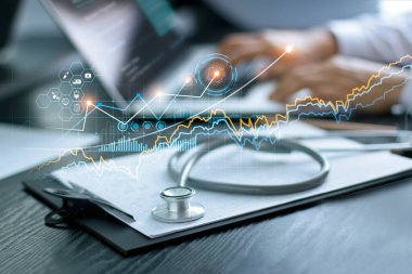 Sağlık hizmetleri grafik verileri ve büyümesi, doktorların sağlık raporlarıyla steteskop masadaki pano, sağlık muayenesi ve laptop ekranındaki tıbbi raporu analiz eden doktor