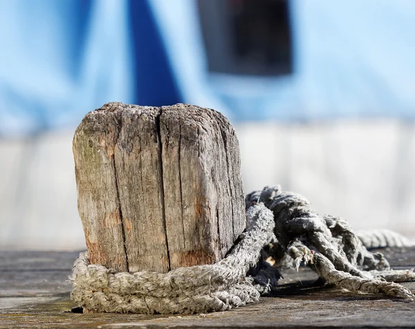 Trä pollare, rep och blå fiskebåtar i bakgrunden — Stockfoto