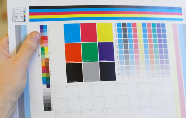 Hand holding a colorful test print for inspection — Stock Photo, Image