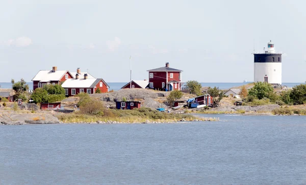 Lighthouse and some small red cottages on a tiny island in the s — Stock Photo, Image