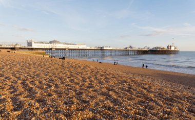 Brighton, İngiltere - 24 Şubat 2017: Ilık akşam ışığında Brighton iskelesi, kumsalda yürüyen uzak insanlar. Ön planda çakıl taşları. 24 Şubat 2017, Brighton, İngiltere