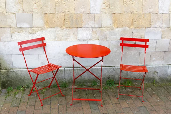 Two chairs and a red table in front of a gray stone wall — Stock Photo, Image