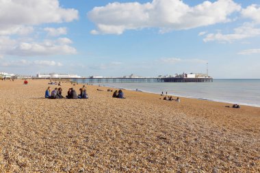 BRIGHTON, GREAT BRITAIN - FEB 24, 2017: People sitting in groups on the Brighton beach. The Brighton pier in the background. February 24, 2017 in Brighton, Great Britain