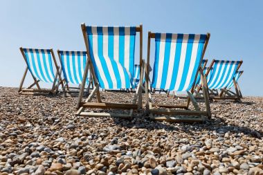 Klasik çizgili mavi ve beyaz şezlonglar çakıl plajı üzerinde bir