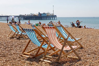 Brighton, İngiltere - 17 Haziran 2017: Klasik şezlonglar ve Brighton rıhtımında güneşlenen insanlar. 17 Haziran 2017, Brighton, İngiltere
