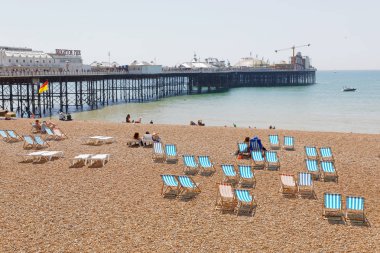 Brighton, Büyük Britanya - 17 Haziran 2017: Klasik şezlonglar ve güneş banyosu Brighton pier çakıl plaj bir güneşli insanlar gün. 17 Haziran 2017 Brighton, Büyük Britanya