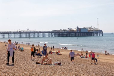 Brighton, İngiltere - 17 Haziran 2017: Brighton sahilinde güneşlenen insanlar, Brighton rıhtımında arka planda. 17 Haziran 2017, Brighton, İngiltere