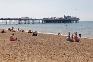 Brighton, İngiltere - 17 Haziran 2017: Brighton sahilinde güneşlenen insanlar, Brighton rıhtımında arka planda. 17 Haziran 2017, Brighton, İngiltere