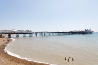 Brighton, İngiltere - 17 Haziran 2017: Brighton sahilinde güneşlenen insanlar, Brighton rıhtımında arka planda. 17 Haziran 2017, Brighton, İngiltere