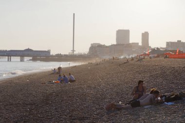Brighton, İngiltere - 17 Haziran 2017: Günbatımında Brighton sahilinde insanlar, arka planda Brighton iskelesi. 17 Haziran 2017, Brighton, İngiltere