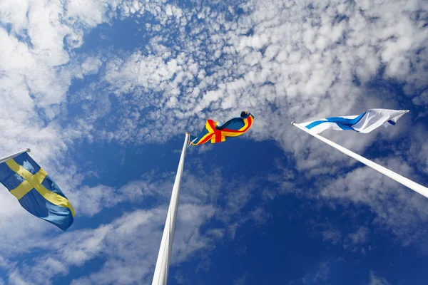 Flags from Sweden, Aland and Finland on flag poles, blue sky and white cloudes
