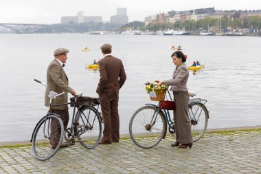 Stockholm - 23 Eylül 2017: Bir kadın ve iki erkek Stokholm, İsveç'te eski moda tüvit kıyafetler ve holding Bisiklet 1960'larda ayakta 23 Eylül 2017 Tweed olay Bisiklet göle yakın gelen giyinmiş