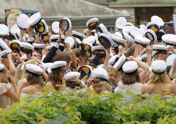 Руки держат много шведских белых выпускных шапок, зеленые деревья в
