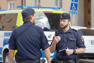 İki İsveçli erkek polis tartışırken önünde bir polis memuru