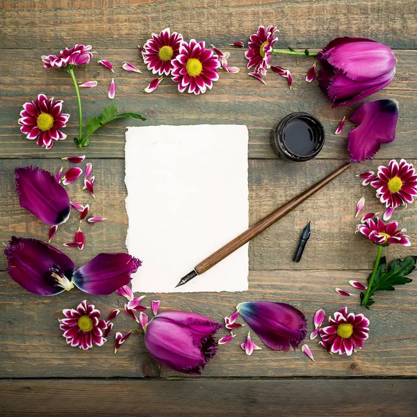 Vintage sheet of paper with dip pen and inkstand surrounded by tulips and daisies on wooden background