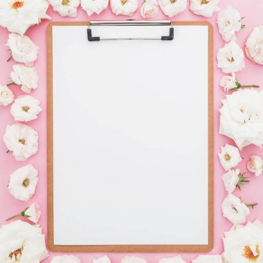 Pembe bir arka plan üzerinde beyaz gül ile çevrili boş kağıdın